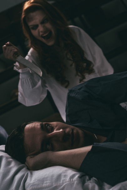 obsessed yelling girl with knife standing over scared man in bed - Photo, Image