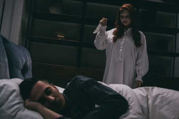 démoni hátborzongató lány késsel áll felett alvó férfi a hálószobában  - Fotó, kép