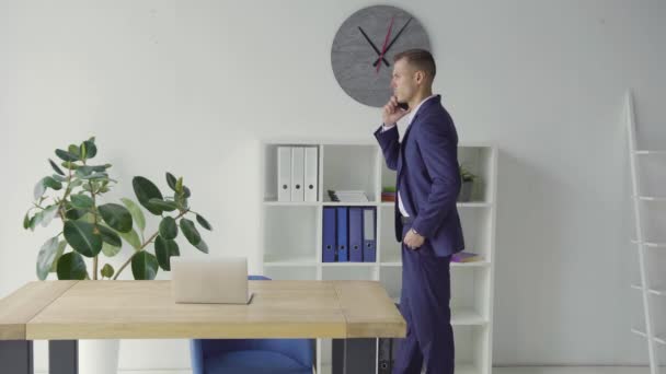Serious business man in blue suit speaking by mobile phone at stylish office. Focused and stressed guy talking phone emotionally at remote workplace. - Imágenes, Vídeo