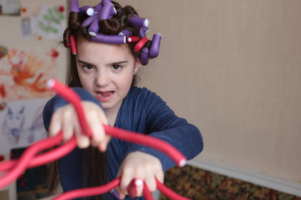 Beautiful cheerful girl of eight years spins curlers on long hair - Photo, Image