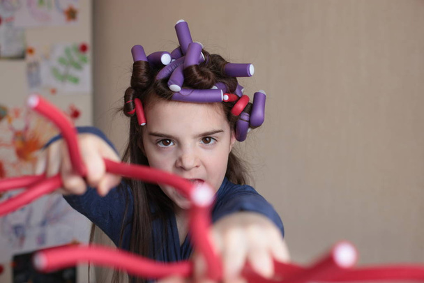 Beautiful cheerful girl of eight years spins curlers on long hair - Φωτογραφία, εικόνα
