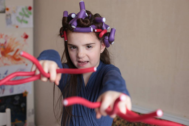 Menina alegre bonita de oito anos gira encrespadores no cabelo longo
 - Foto, Imagem