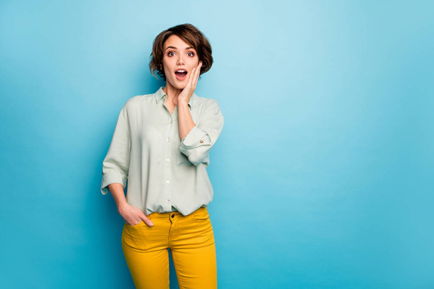 Photo of funny beautiful lady short hairdo look open mouth read discount banner advert arm on chin wear casual green shirt yellow trousers isolated blue color background - Фото, зображення