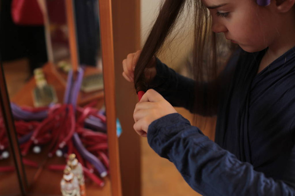 Schöne fröhliche Mädchen von acht Jahren dreht Lockenwickler auf langen Haaren - Foto, Bild