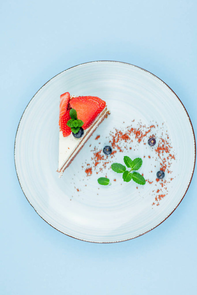 Un bel pezzo di torta con bacche con crema di burro su sfondo blu. Torta con torte rosse
. - Foto, immagini