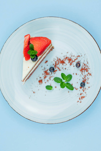 Ein schönes Stück Kuchen mit Beeren und Buttercreme auf blauem Hintergrund. Kuchen mit roten Kuchen. - Foto, Bild