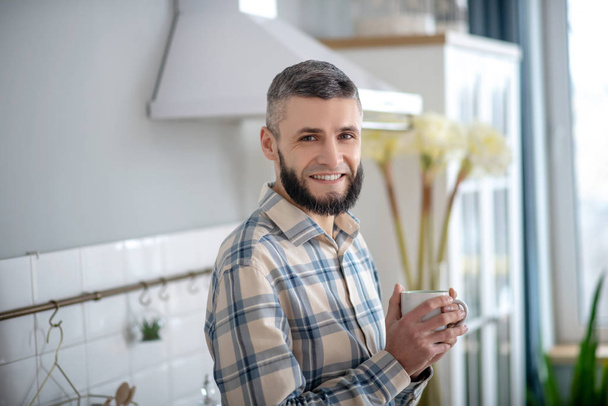 Smiling young bearded man standing with a white cup. - Foto, afbeelding