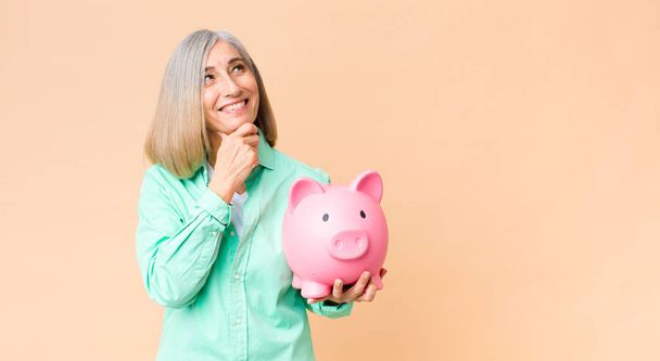 middle age pretty woman holding a piggy bank against copy space wall - Foto, immagini