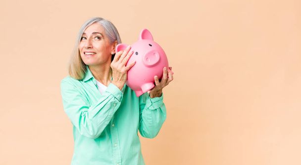 middle age pretty woman holding a piggy bank against copy space wall - Foto, immagini