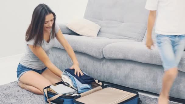 Mom is packing a huge blue suitcase. Little boy is carrying her clothes to put in suitcase. Getting ready for travel. 4K. - Materiał filmowy, wideo