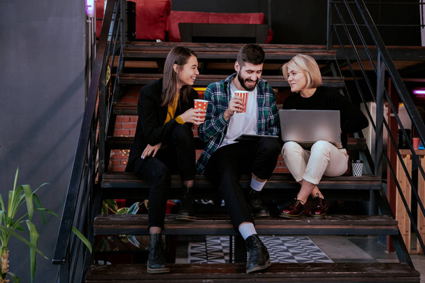 Drie charismatische jonge kantoormedewerkers die hard werken met tablet en notebook om het werkplan te analyseren terwijl ze op een kantoortrap zitten - Foto, afbeelding