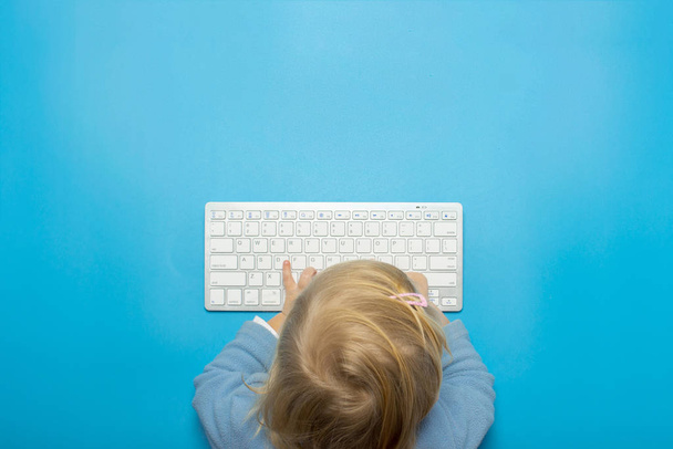 Das kleine Kind hält die Hände auf der Tastatur auf blauem Hintergrund. Draufsicht, flache Lage - Foto, Bild