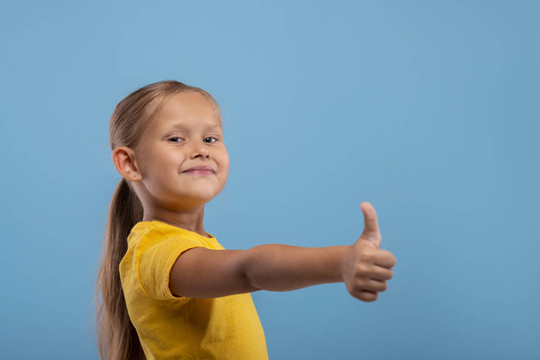 ein junges lächelndes Mädchen gibt dir eine zustimmende Geste gegen blu - Foto, Bild