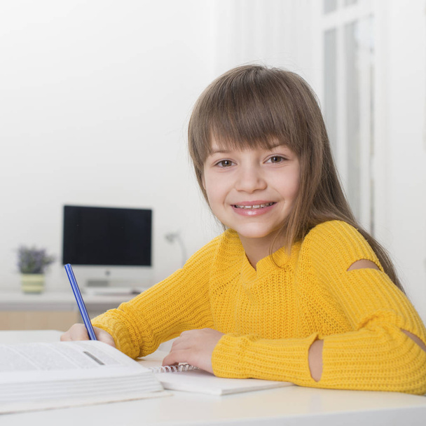eine blonde Schülerin sitzt zu Hause an einem Tisch und macht Hausaufgaben  - Foto, Bild