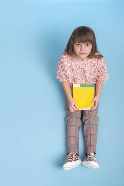 Молода дівчина сидить з книгою в руках на синьому фоні
 - Фото, зображення