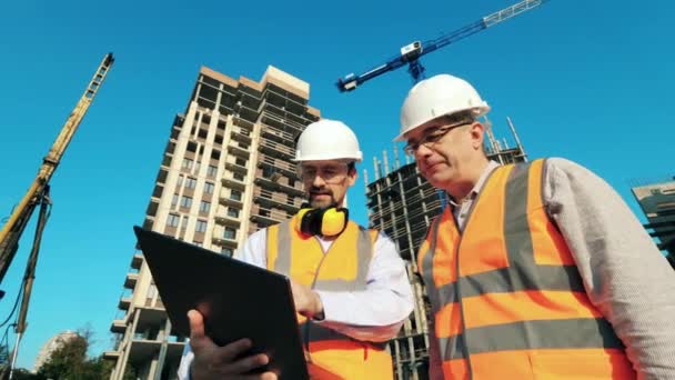 Working engineers, construction architects discussing construction plan using laptop while standing on a building site. - Footage, Video