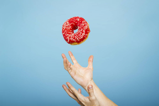 Hände fangen einen Donut mit Zuckerguss. Blauer Papphintergrund. Konzept des Backens, handgemacht. Flache Lage, Draufsicht - Foto, Bild