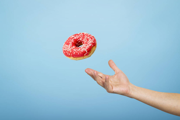 Mão pegar um donut com gelo vermelho. Fundo de papelão azul. O conceito de cozimento, feito à mão. Deitado plano, vista superior
 - Foto, Imagem
