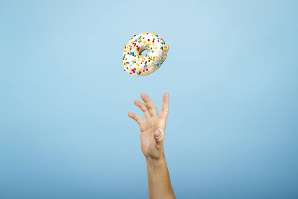 Hand fangen einen Donut mit Zuckerguss. Blauer Papphintergrund. Konzept des Backens, handgemacht. Flache Lage, Draufsicht - Foto, Bild