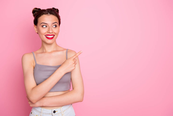 Photo of pretty millennial lady pretty buns red pomade indicating finger empty space advising best shopping prices wear casual grey short top isolated pink color background - Foto, immagini