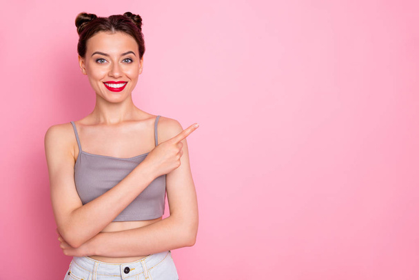 Photo of pretty youngster lady pretty buns red pomade indicating finger empty space advising best shopping prices wear casual grey short top isolated pink color background - Photo, image