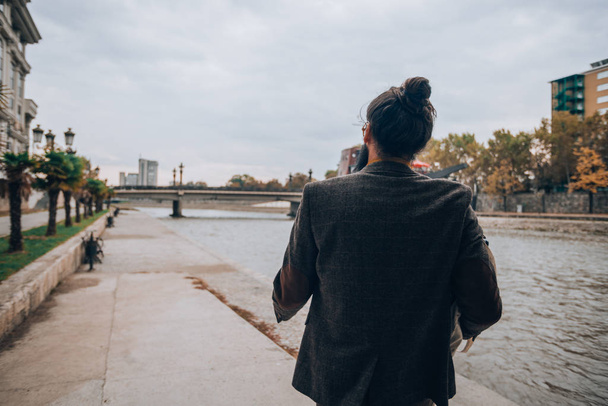 A handsome young hipster dressed in modern style clothes at a river walkway - Фото, изображение