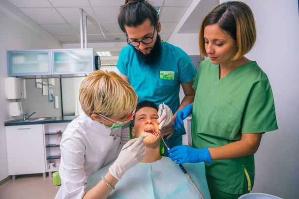 Profesionální tým zubních lékařů pomáhá při zubní prohlídce mladého chlapce pacienta - Fotografie, Obrázek