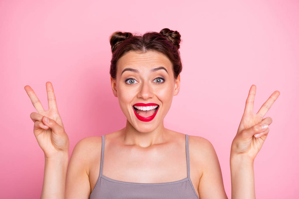 Hi party people. Photo of amazing youngster lady funny buns red lipstick showing v-sign symbol wear casual grey tank-top isolated pink color background - Φωτογραφία, εικόνα