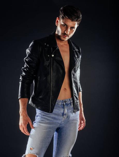 Attractive man posing in ripped blue jeans and fancy leather jacket - Foto, Bild