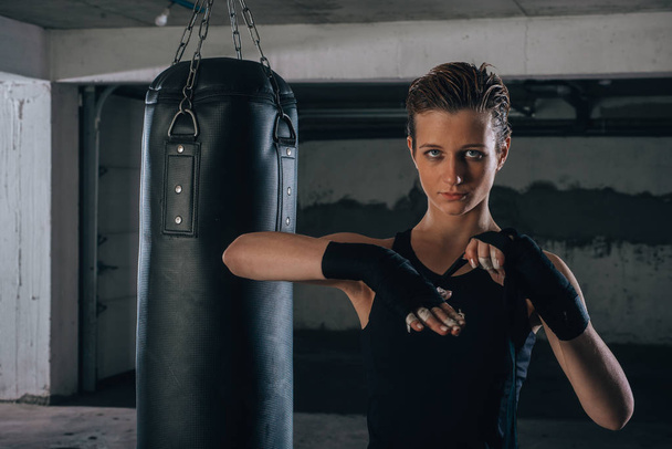 写真の焦点を当てた若い女性準備彼女の黒包帯のためにボクシングのためにガレージ. - 写真・画像