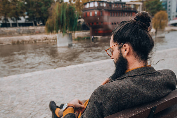 Giovane uomo d'affari moderno che indossa abiti di classe su una panchina sulla passerella del fiume della città
 - Foto, immagini