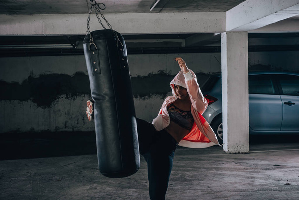 Young sportswoman doing high kick during boxing exercise in a garage. - 写真・画像