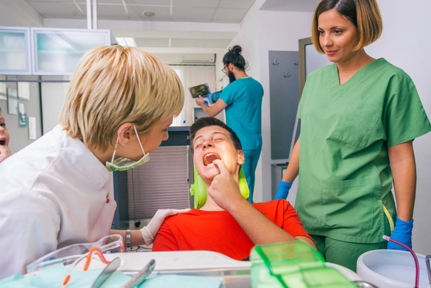 Dentista femminile con l'aiuto del suo dentista tecnico esamina la bocca e i denti di un adolescente paziente ragazzo. - Foto, immagini