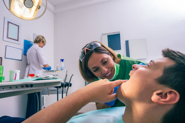 Close-up beeld van een tiener jongen patiënt tonen zijn kiespijn aan zijn vrouwelijke tandarts in de tandartspraktijk. - Foto, afbeelding