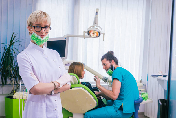 Junge Zahnärztinnen stehen mit verschränkten Händen im weißen Kittel am Arbeitsplatz. - Foto, Bild