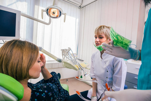 Close up portrait of a beautiful young lady sitting in the dental chair while stomatologist ( dentist ) with hands in sterile gloves is fixing her teeth. - Photo, Image