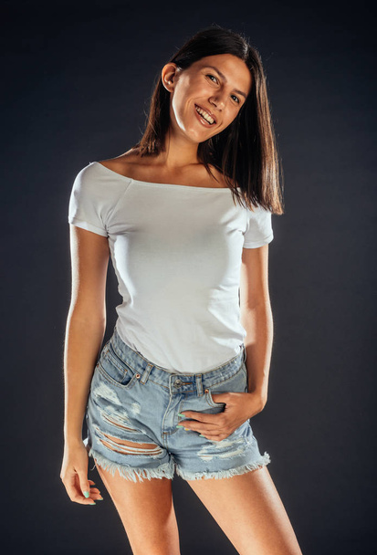 Πορτρέτο μιας ελκυστικής γυναίκας που ποζάρει σε λευκό μπλουζάκι και σκίζει κοντά τζιν - Φωτογραφία, εικόνα