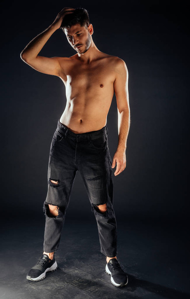 Trendikäs paidaton mies poseeraa mustissa housuissa ja urheilukengissä
 - Valokuva, kuva