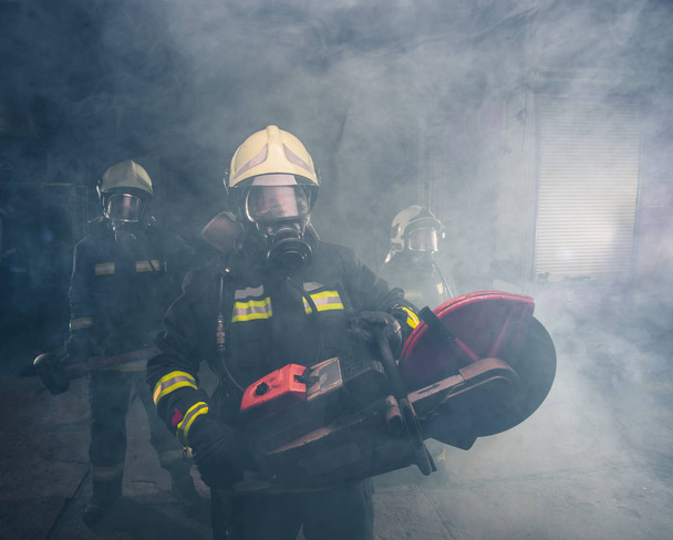 Portrait d'un pompier tenant une scie à chaîne de sauvetage dans un garage enfumé - Photo, image