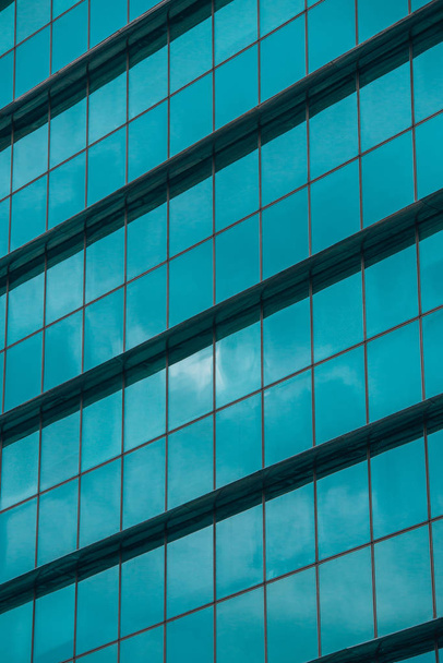 Висотна офісна будівля з блакитною скляною стіною, що відображає небо і хмари
 - Фото, зображення