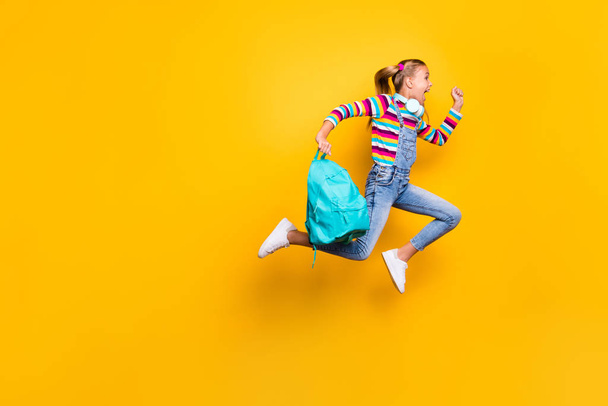 Full body profile side photo crazy schoolchild jump run school discounts hold blue bag rucksack wear striped sweater denim jeans suspenders overalls isolated bright shine yellow color background - Фото, зображення