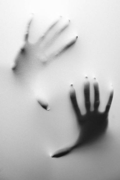 Eine vertikale Graustufenaufnahme der Hände einer Person hinter einem gefrorenen Glas - Konzept der Angst und der bösen Träume - Foto, Bild