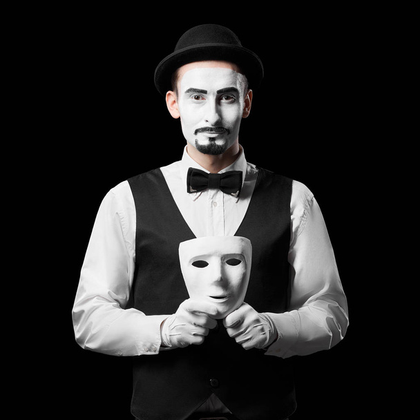 Mime artist holding white mask. Isolated on black background. Concept of people masks and lies - Photo, Image