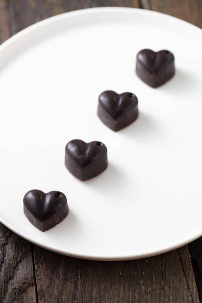 Un colpo vista dall'alto di cioccolatini a forma di cuore nero sulla piastra bianca
 - Foto, immagini