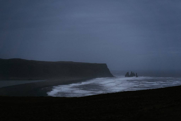 A beautiful scenery of the sea waves surrounded by rocky hills covered with fog in Iceland - Foto, Imagen