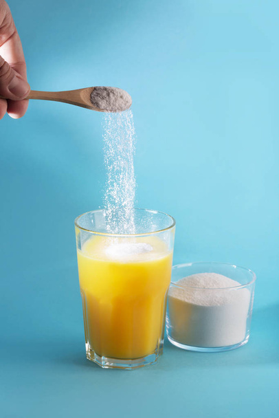 A glass juice and a spoon with collagen powder on blue background. - Photo, image