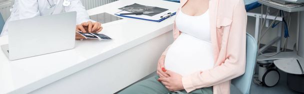 tiro panorâmico de médico profissional mostrando varredura de ultra-som para a mulher grávida jovem na clínica
 - Foto, Imagem