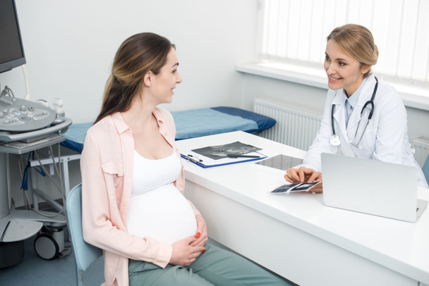 médico sorrindo mostrando ultra-som varredura para a mulher grávida jovem na clínica
 - Foto, Imagem