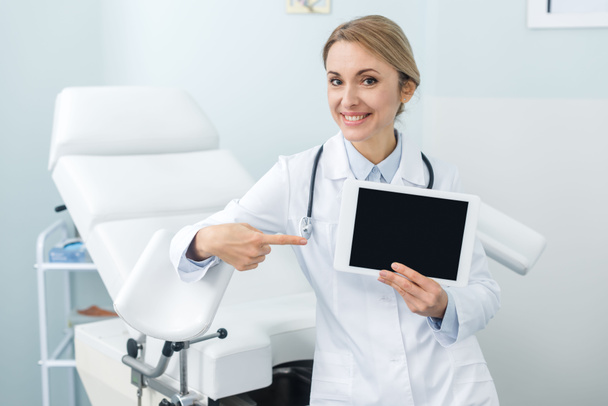 χαμογελαστός γυναικολόγος δείχνει σε ψηφιακή ταμπλέτα με λευκή οθόνη στην κλινική - Φωτογραφία, εικόνα