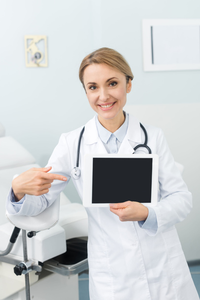 Gülümseyen kadın jinekolog klinikte boş ekranla dijital tableti işaret ediyor. - Fotoğraf, Görsel